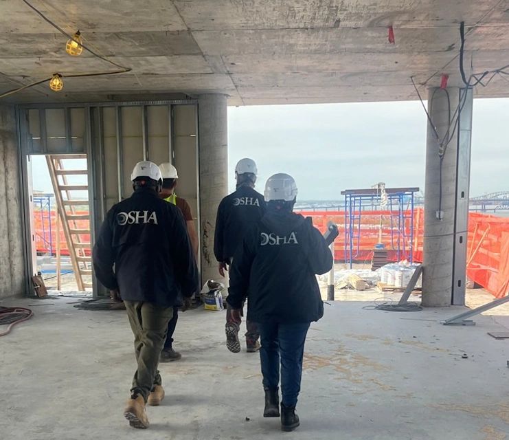 OSHA compliance officers in agency jackets walking through an active construction site